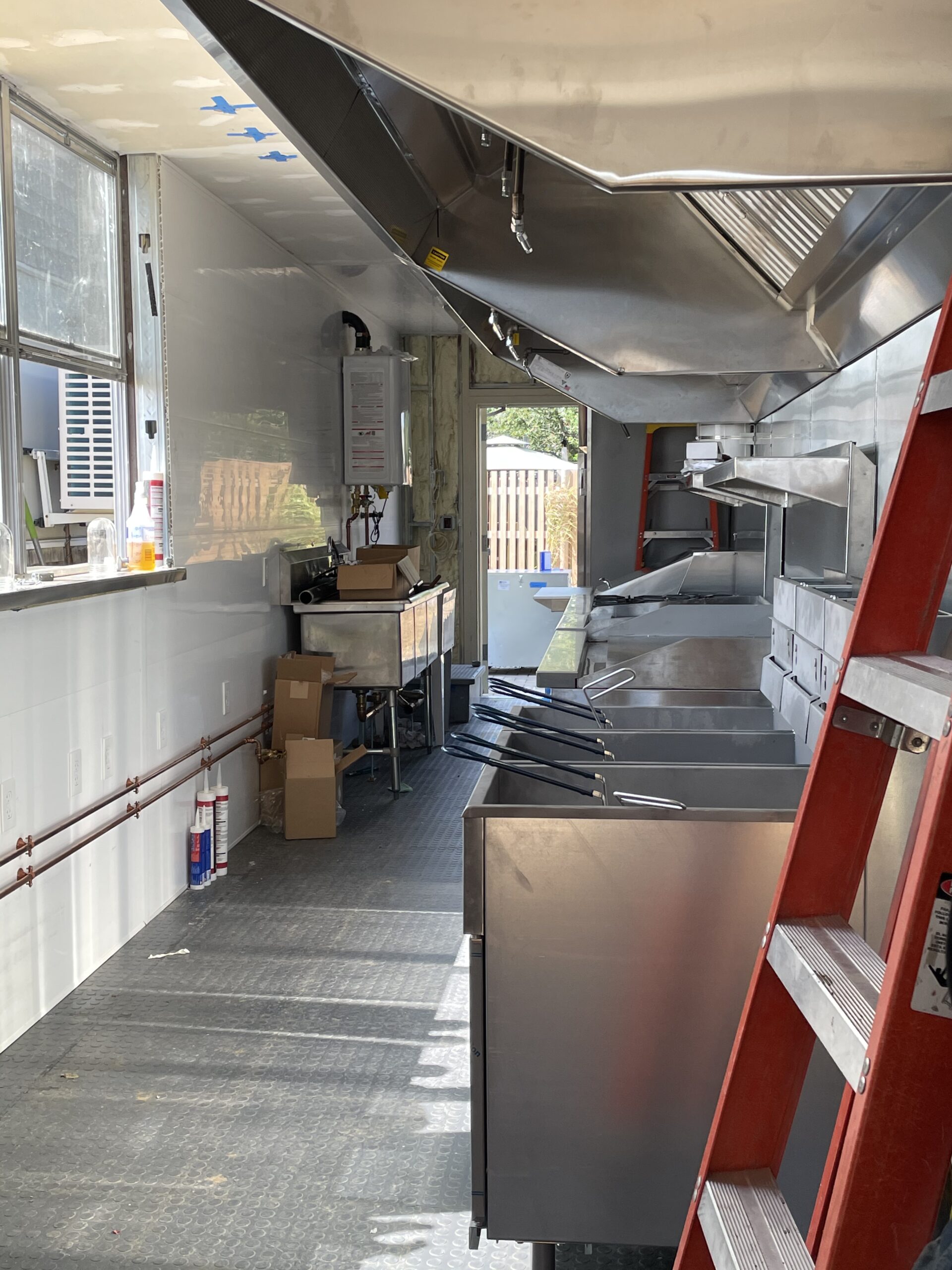 Interior of a commercial food truck kitchen with stainless steel equipment, ventilation hood, and storage boxes, showcasing the setup for food preparation and service in Plaistow, NH.
