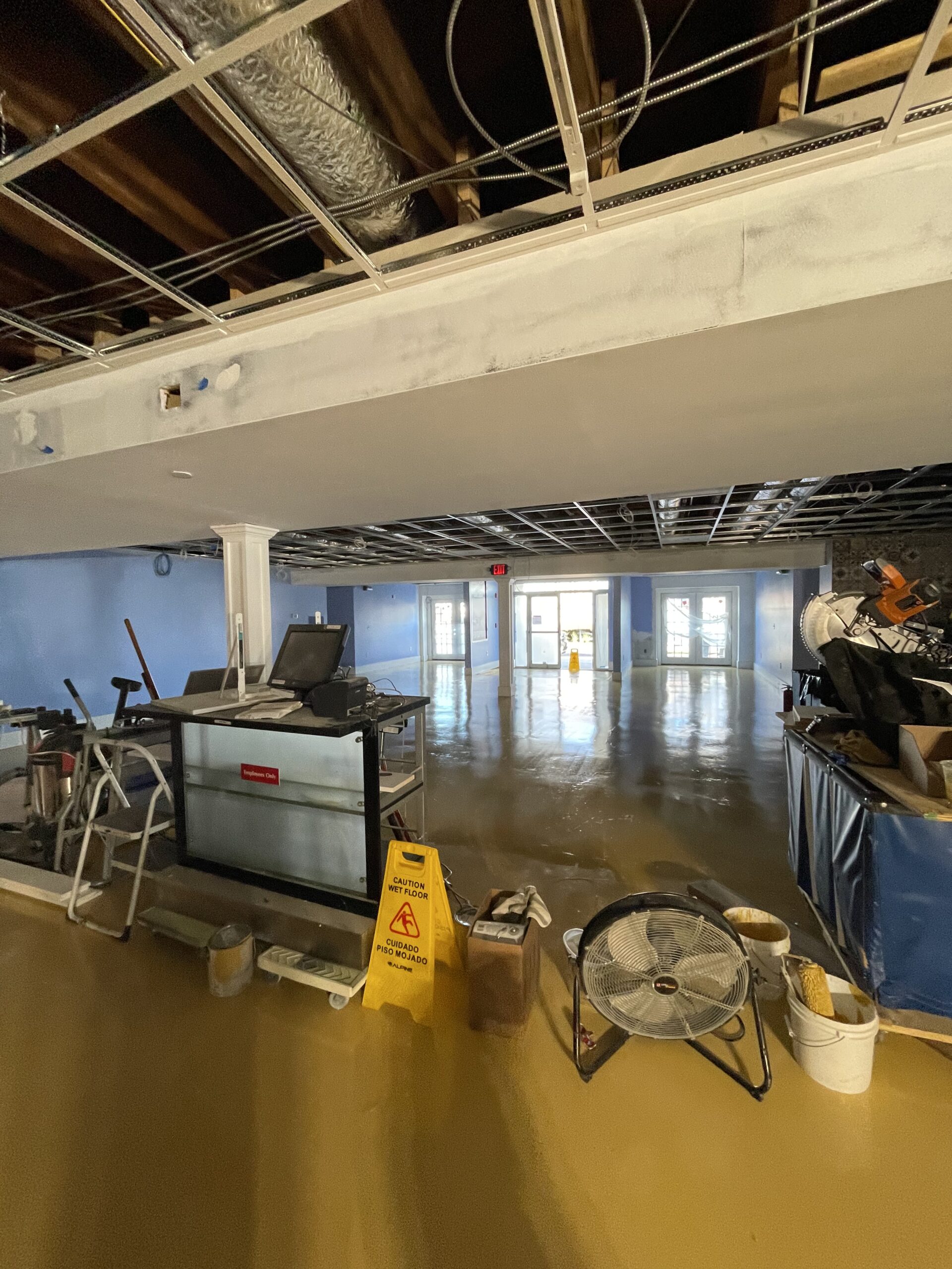Commercial space under renovation with visible electrical equipment, caution wet floor sign, and unfinished flooring, indicative of tenant improvements and electrical service upgrades by Moore Electric.