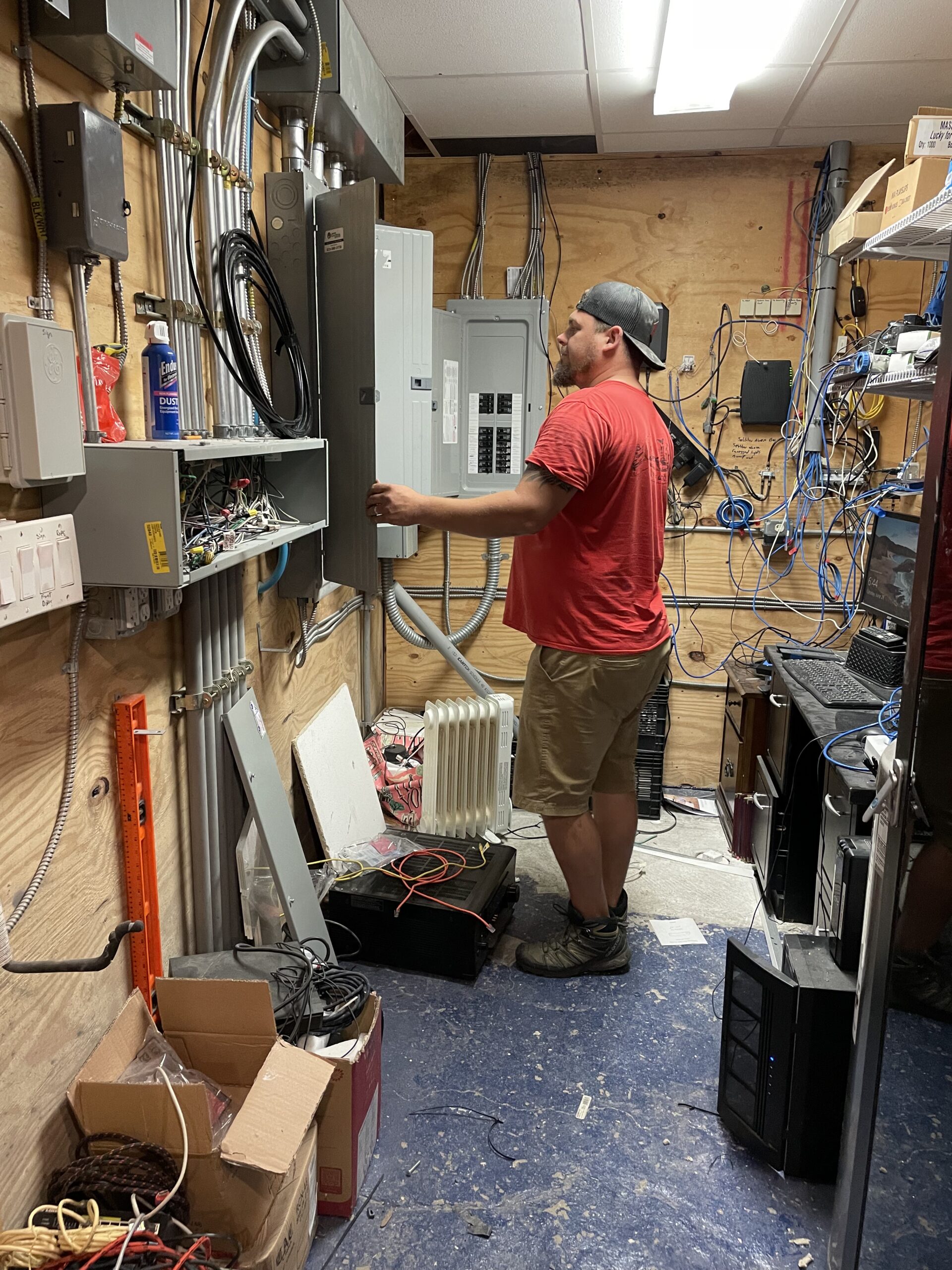 Electrician working on electrical panel installation in a cluttered wiring area, showcasing aluminum wiring remediation techniques relevant to Moore Electric's services.