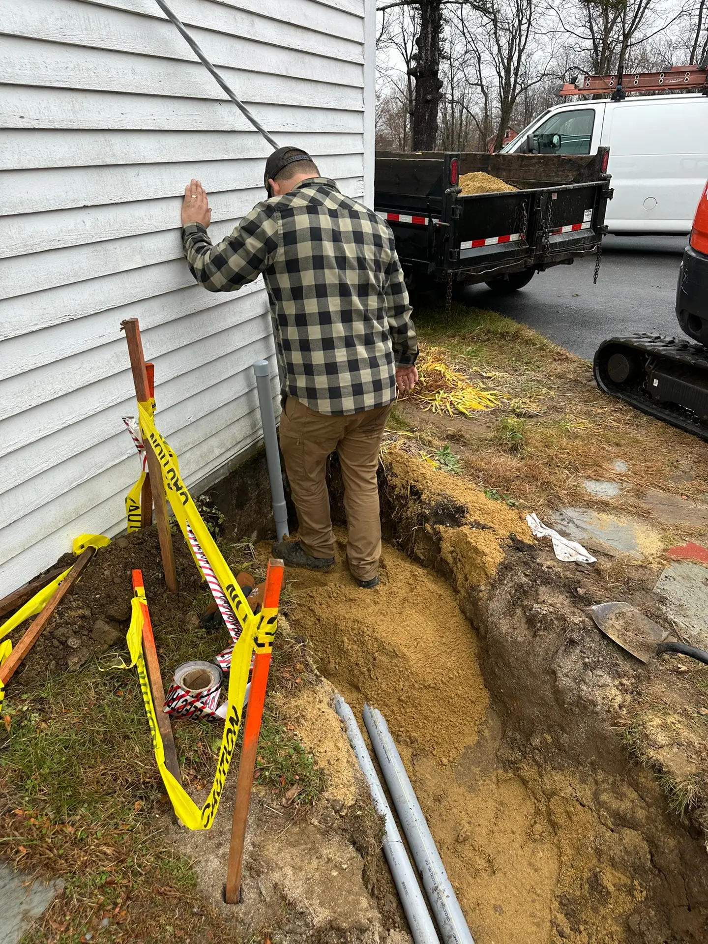 Licensed electrician assessing electrical service entrance repair in trench with caution tape and tools in Plaistow, NH.