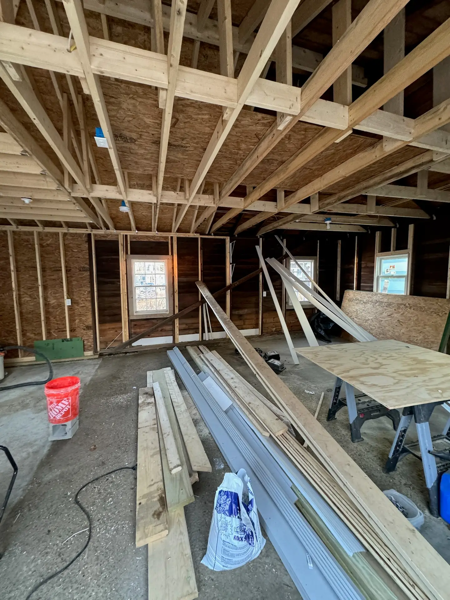 Interior view of a new construction site with exposed wooden framing, construction materials like lumber and drywall, and tools, illustrating the rough-in phase of electrical work by Moore Electric in Plaistow, NH.