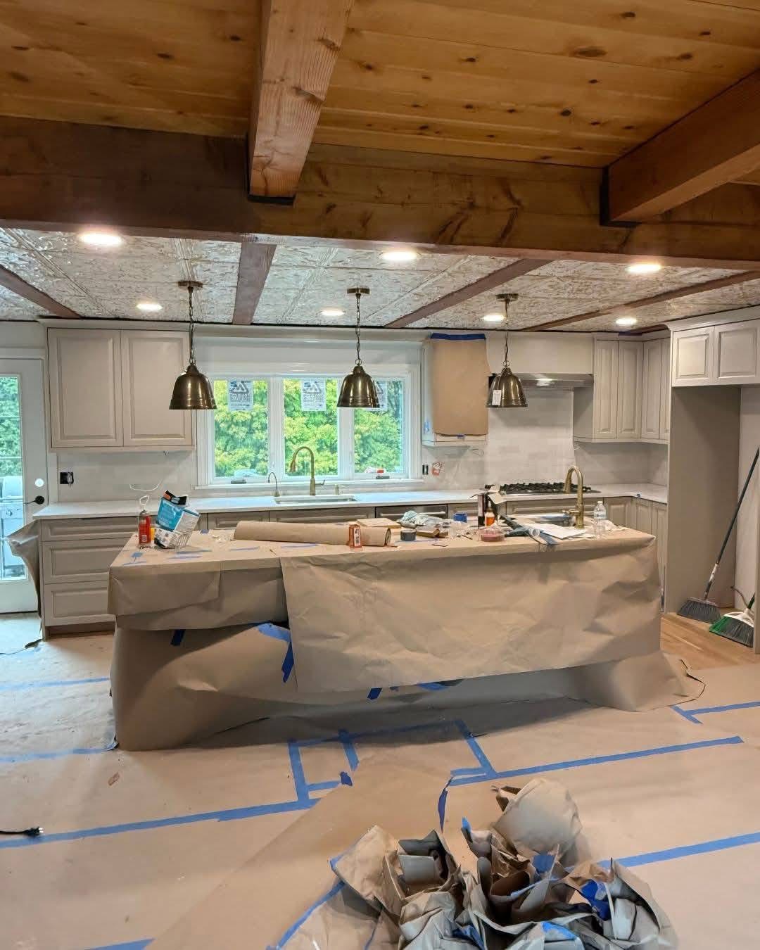 Kitchen renovation in progress featuring an island covered in protective paper, new cabinetry, and modern pendant lighting, illustrating electrical work for a remodel.