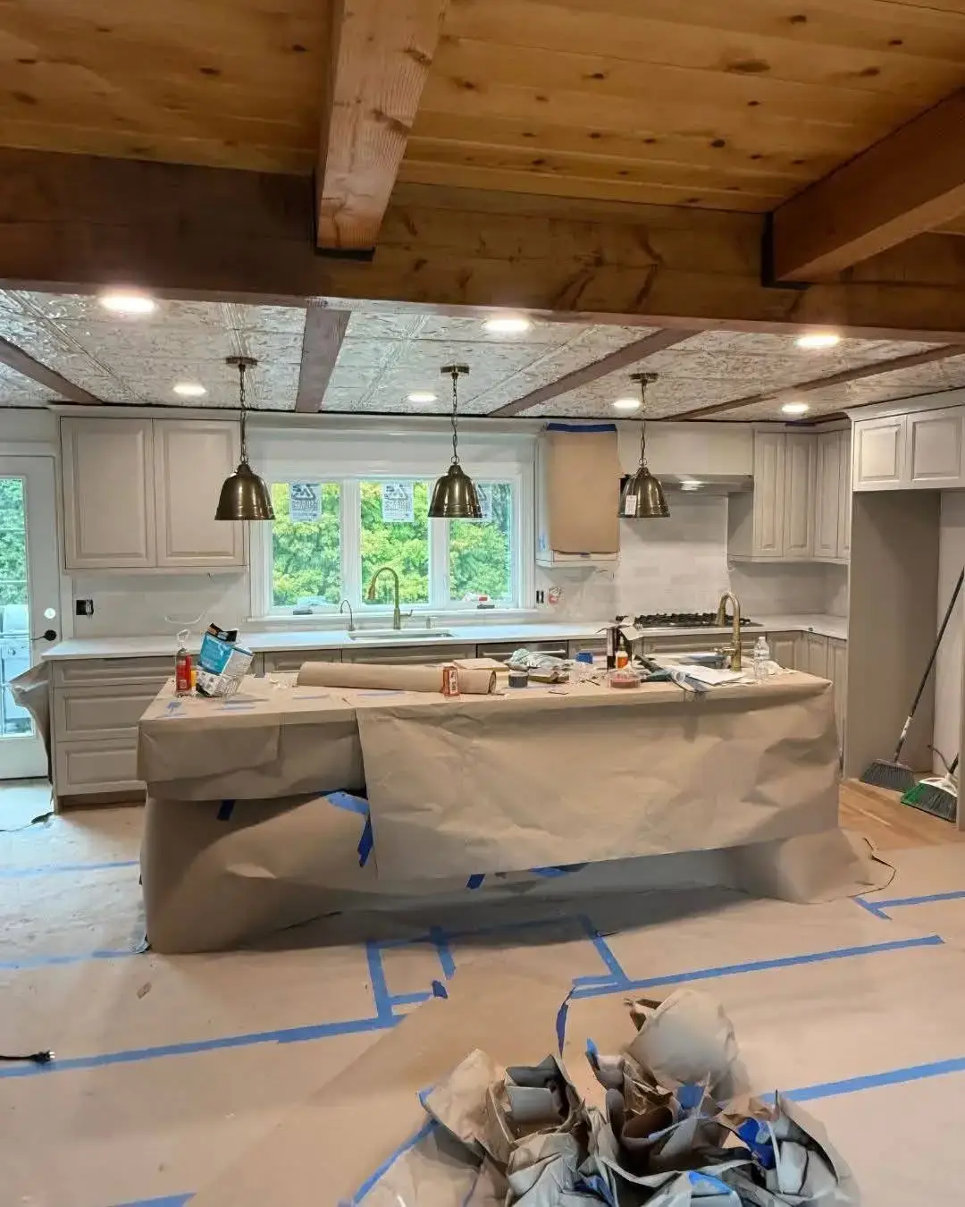 Kitchen remodel in progress with covered countertops, pendant lighting, and organized materials in Plaistow, NH.