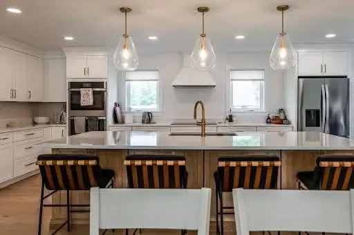 Modern kitchen interior featuring a large island with seating, pendant lighting, stainless steel appliances, and white cabinetry, illustrating electrical upgrades for kitchen renovations by Moore Electric Inc.