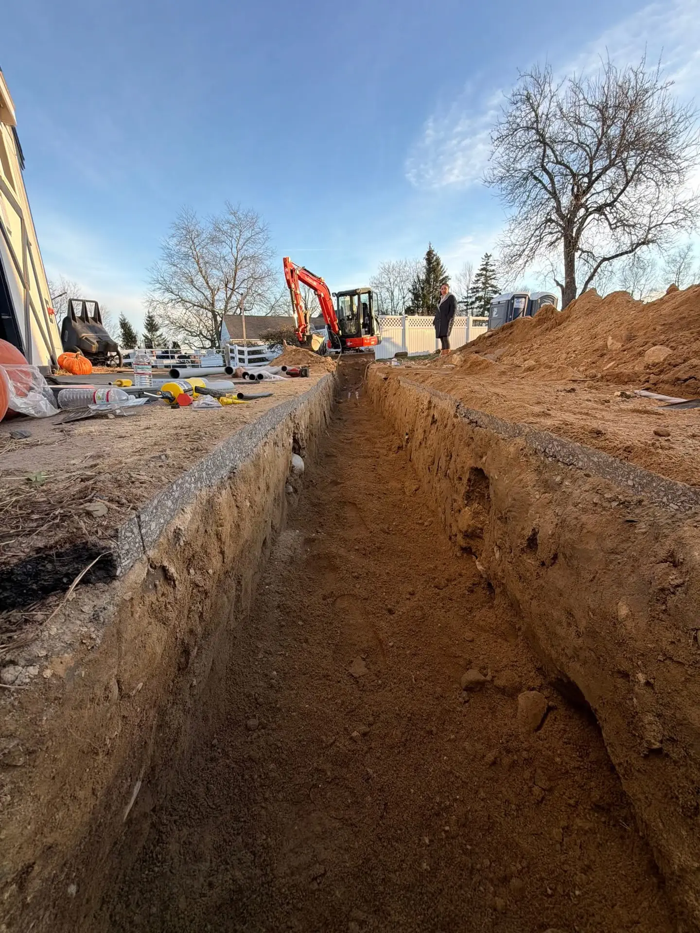 Excavated trench for electrical installation in new construction site, with construction equipment and tools visible, showcasing groundwork preparation for electrical services by Moore Electric in Plaistow, NH.