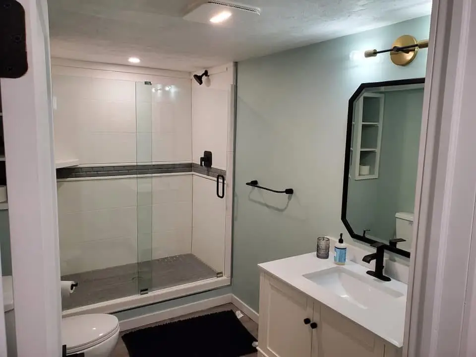 Modern bathroom with glass shower enclosure, white vanity, GFCI outlet, and proper lighting, showcasing compliance with electrical standards for renovations.