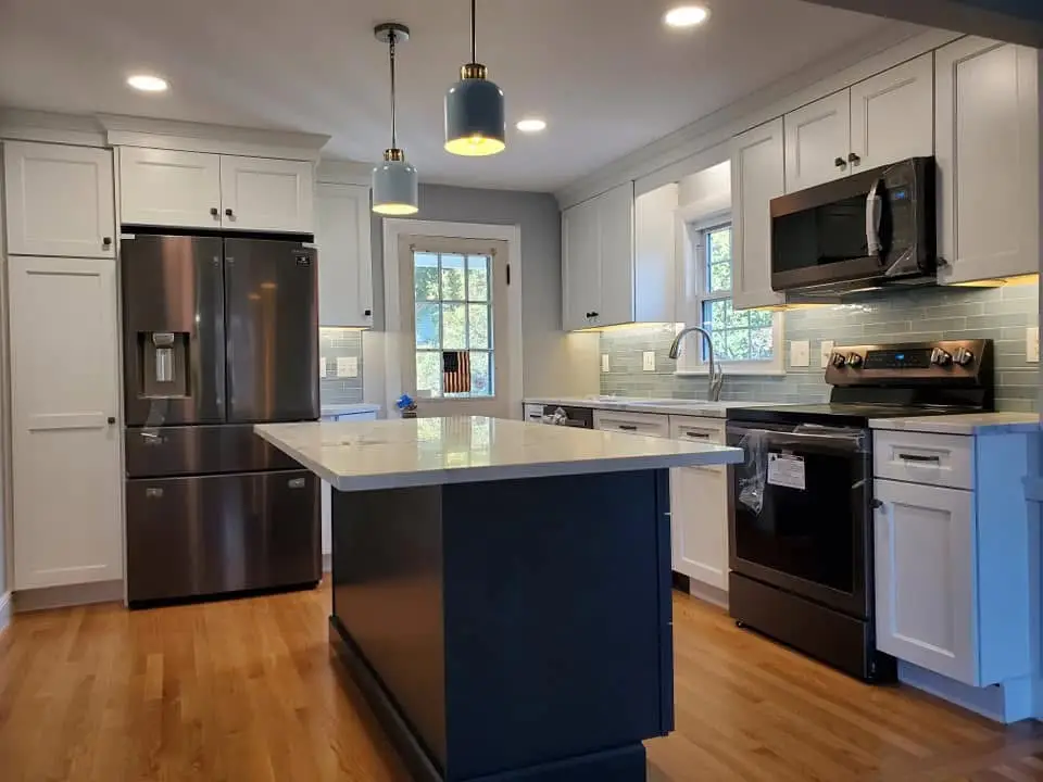 Modern kitchen interior featuring stainless steel appliances, white cabinetry, and an island with a quartz countertop, emphasizing a contemporary design suitable for electrical service upgrades.