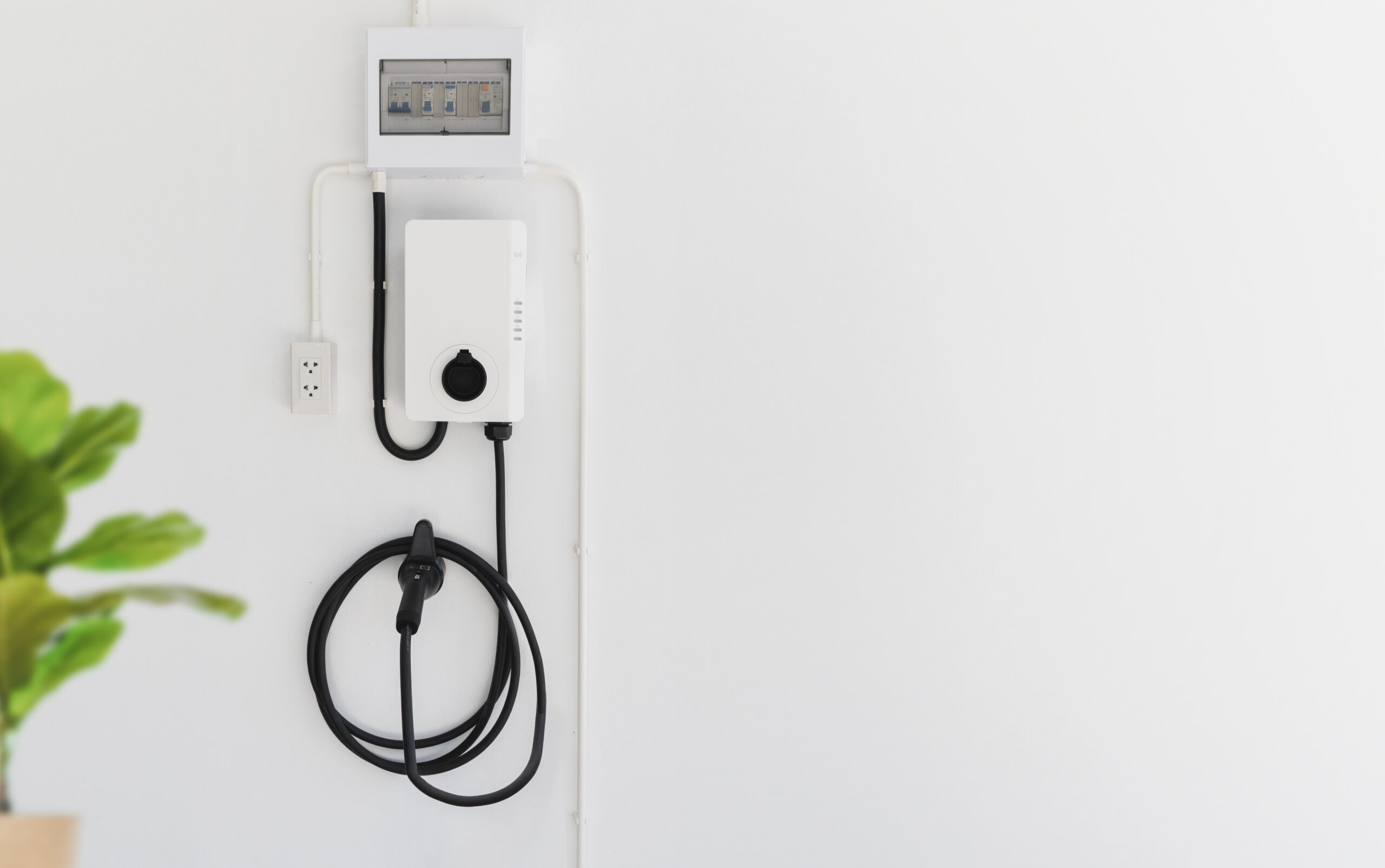 Level 2 EV charger installed on a wall with charging cable and electrical panel, representing home charging solutions for electric vehicles by Moore Electric Inc.