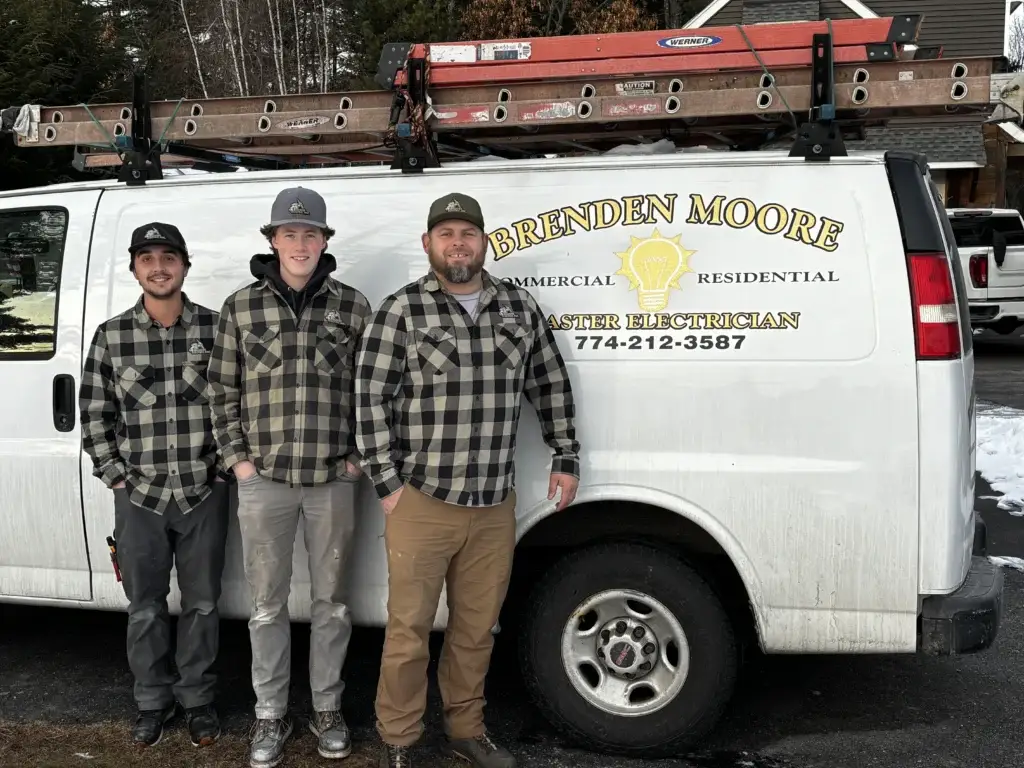 Three electricians in plaid shirts standing in front of a branded van with ladders, representing Moore Electric's reliable electrical repair and troubleshooting services.