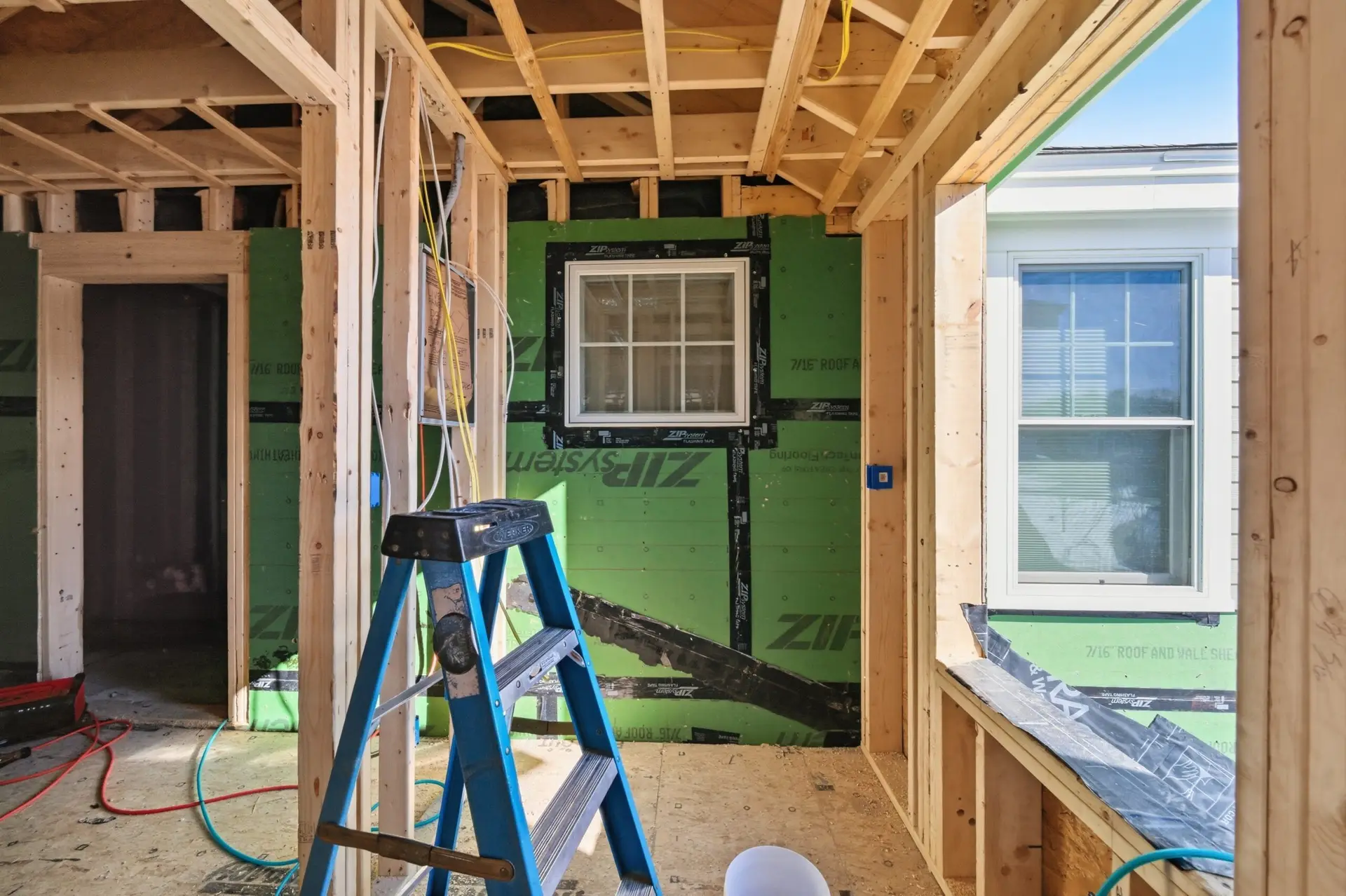 Interior view of a home addition under construction, featuring exposed framing, electrical wiring, and a blue ladder, highlighting the electrical work relevant to home additions in Plaistow, NH.