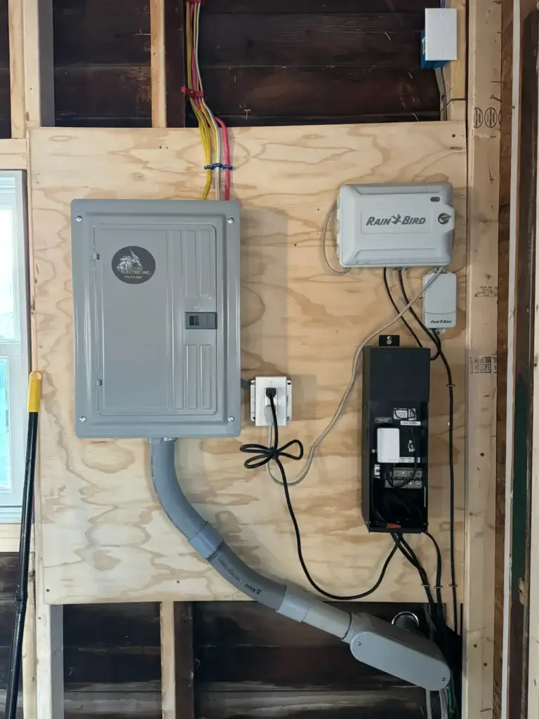 Electrical panel installation with wiring and Rain Bird system on wooden wall, illustrating modern electrical setup and potential rewiring needs.