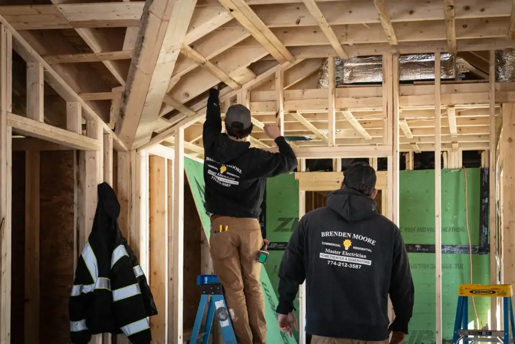 Electricians working on electrical installation in a residential construction site, featuring Brenden Moore branding and safety gear.