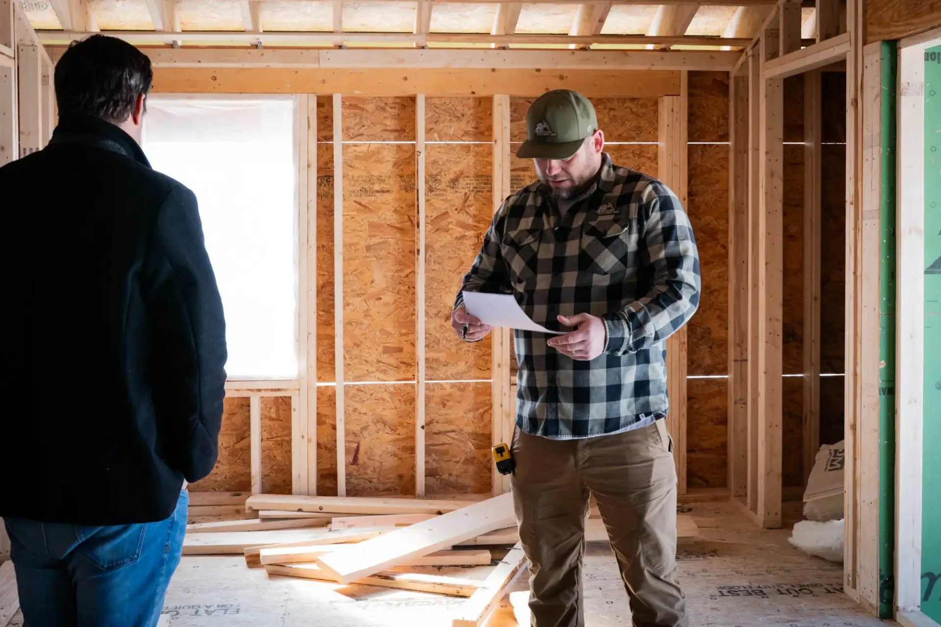 Two electricians discussing plans in a partially constructed room, one holding a document, emphasizing reliable electrical services in Salem, NH.