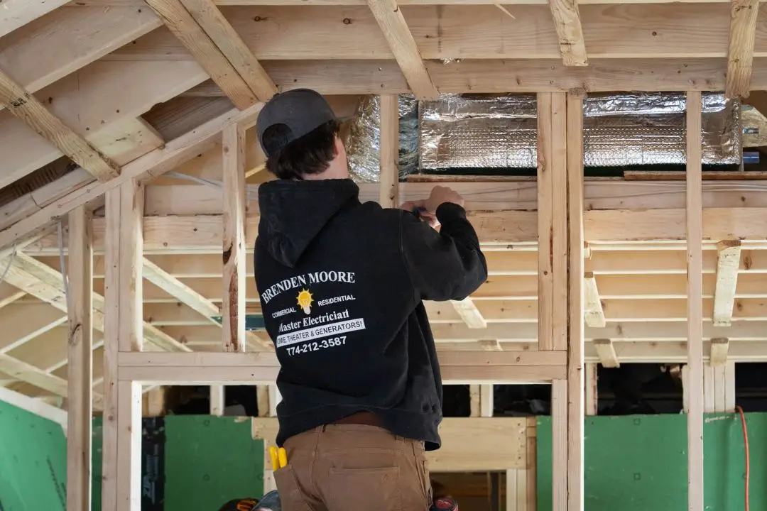 Electrician working on electrical installation in a home addition, showcasing framing and insulation, emphasizing compliance with local building codes in Plaistow, NH.