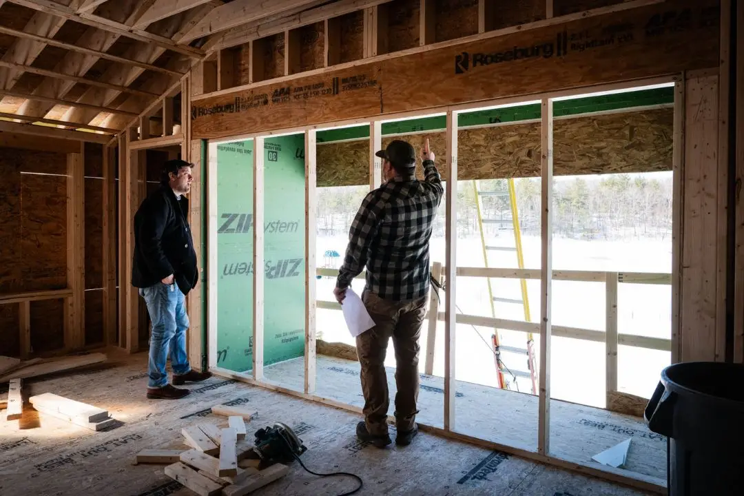 Two electricians discussing installation details in a new residential construction site, featuring wooden framing and insulation materials, emphasizing local expertise in electrical work for new homes in Plaistow, NH.