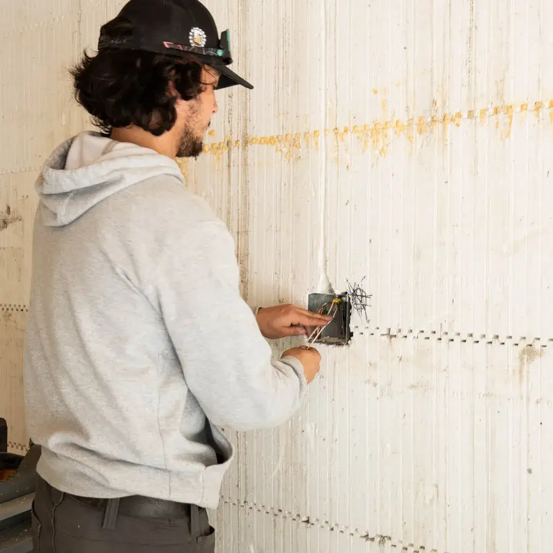 Man installing electrical wires into a junction box on a construction wall.